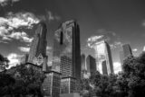 black and white photo of downtown Los Angeles' skyscrapers, with some clouds in the sky reflected back in an imposing manner.